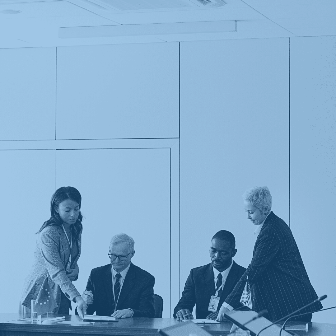 Government employees in a federal building reading documents regarding compliance. Two male employees and two female employees.