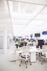 Modern office space with white desks, chairs, and lots of laptops.